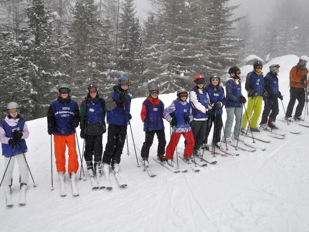 Skigruppe steht in einer Reihe vor verschneiten Bäumen.